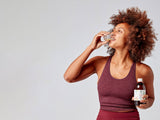 Woman in athletic wear holding a bottle of Multi Strain Biotic and drinking from glass